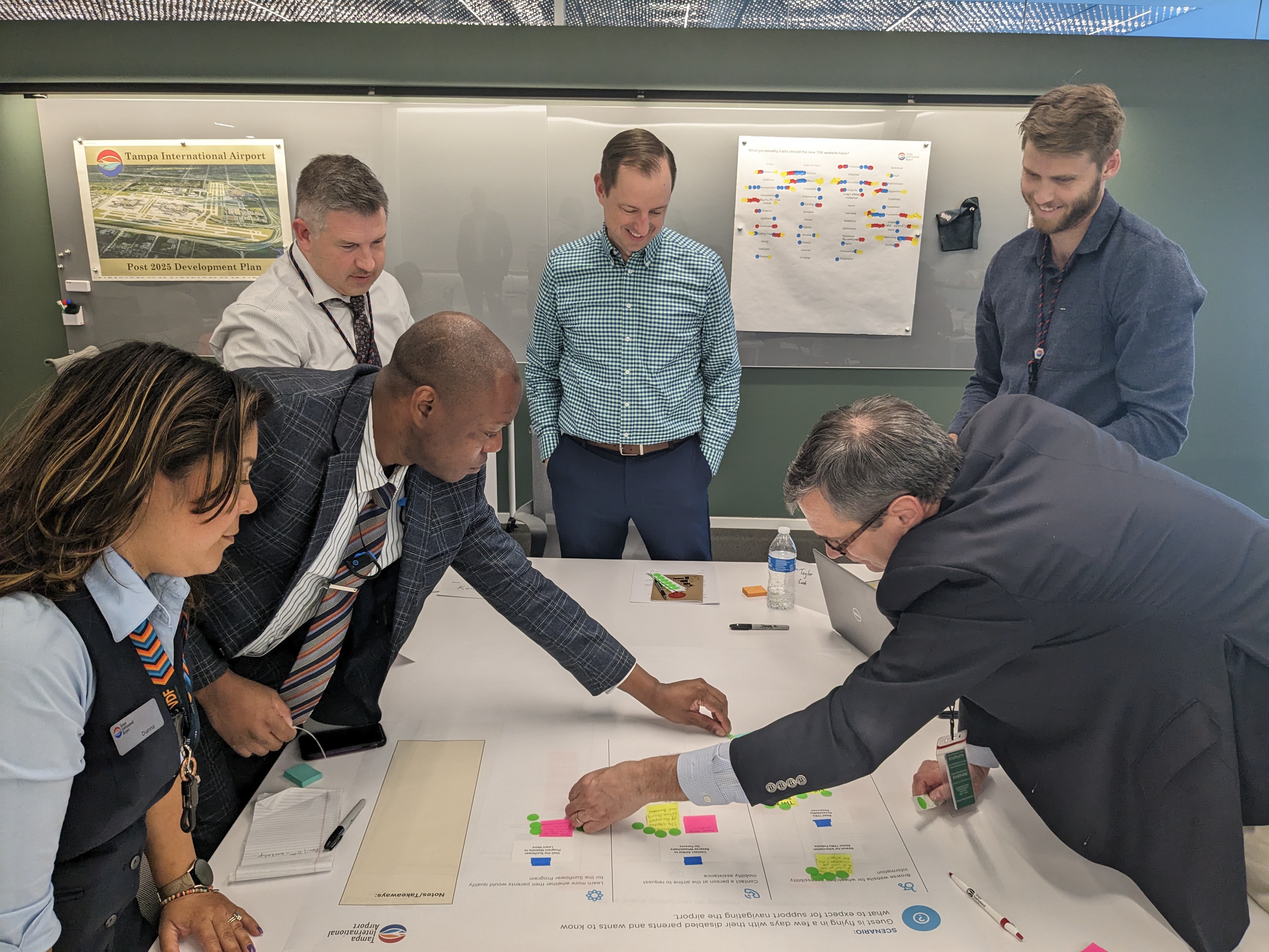Five staff members from Tampa International Airport placing cards on a poster during a UX workshop with an Aten project team member observing