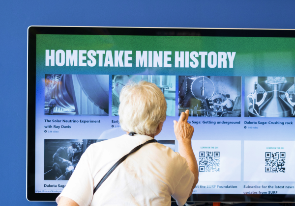 Visitor at SURF interacting with the 'Homestake Mine History' content on the digital kiosks